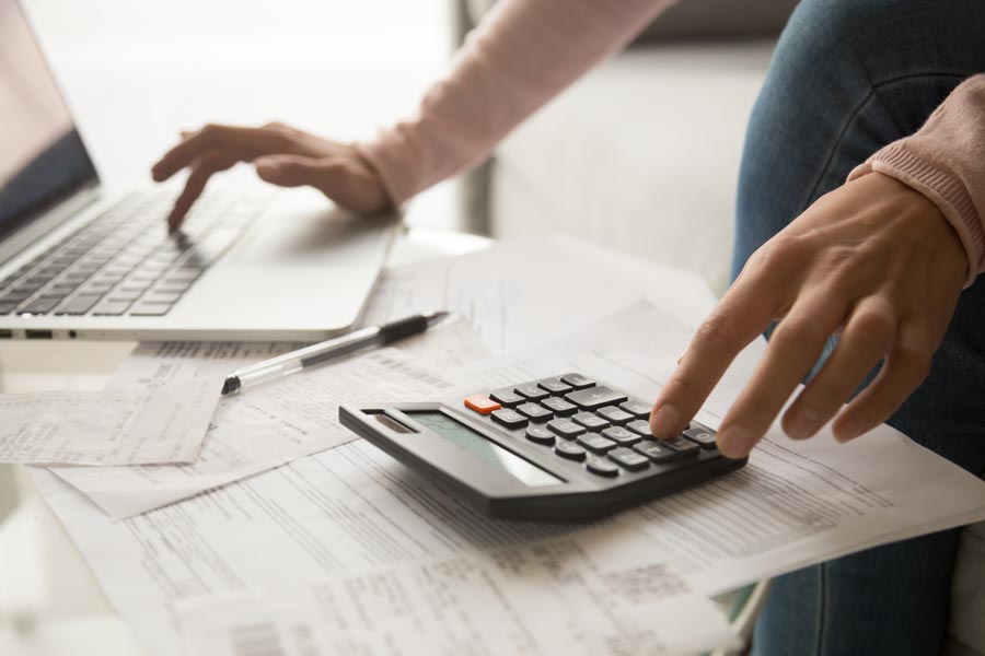 A woman types on her computer while working on a calculator.