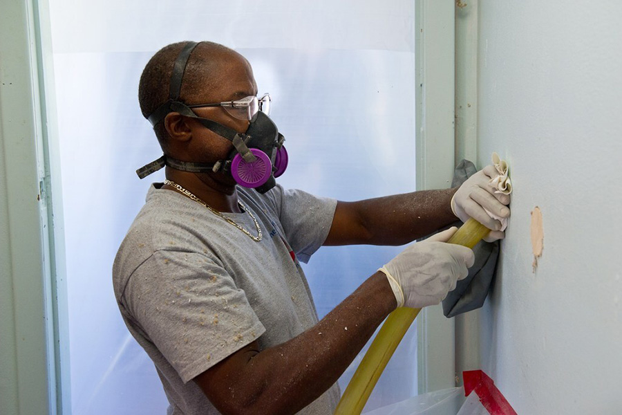 Man wears mask as he uses a device to help install insulation.