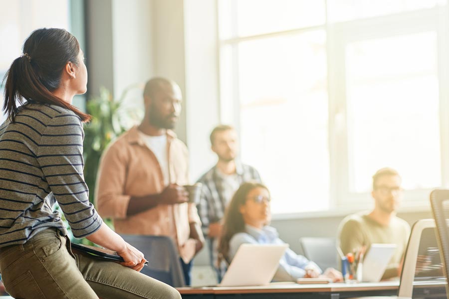 A group of office workers meet in a sunny meeting space.