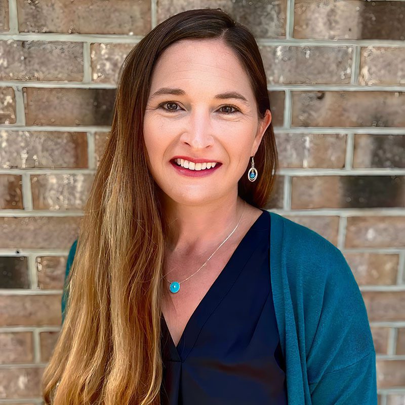 White female standing in front of a brick wall wearing a blue shirt.