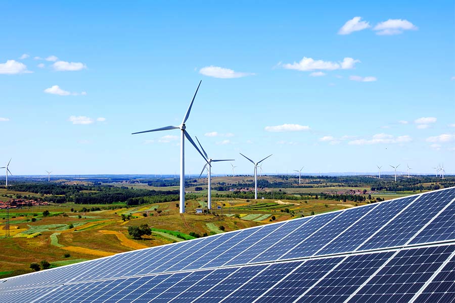 A solar panel in the foreground with windmills in the background on a field.