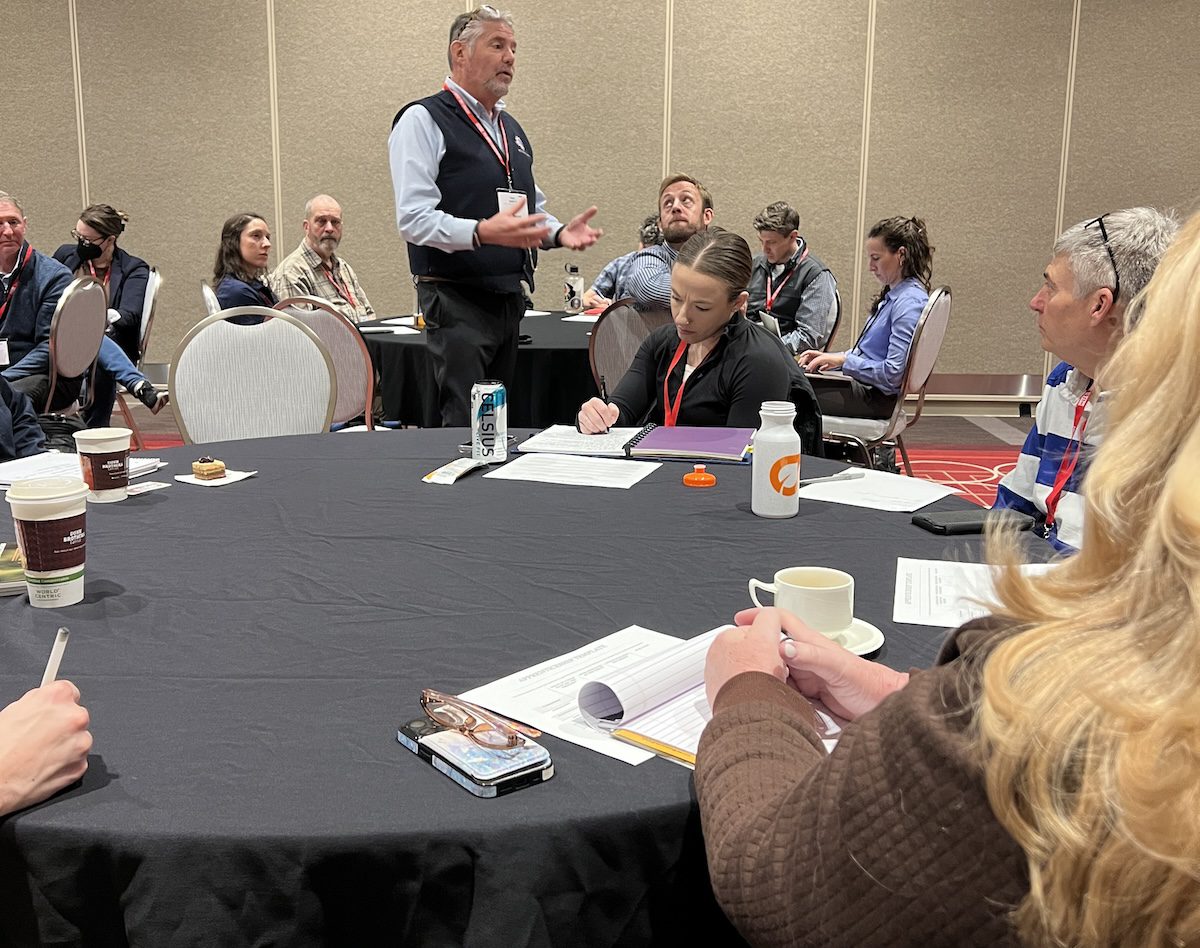 Image of a speaker presenting to groups of people at tables