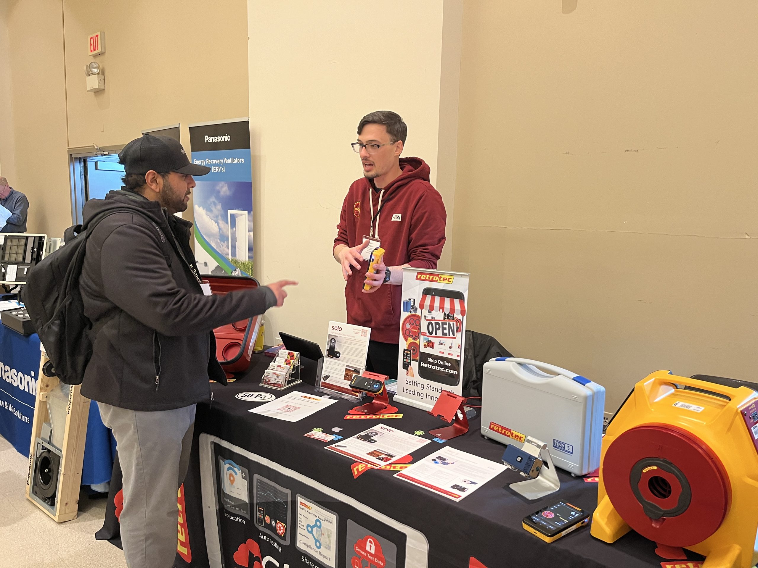 Image of a man at a booth showing another man the various items at the booth
