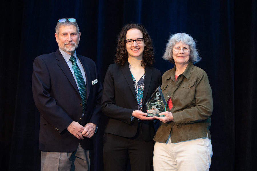 Photo of three individuals, one of which is being handed a trophy