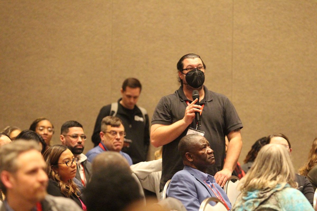 Image of a man asking a question to a speaker into a microphone